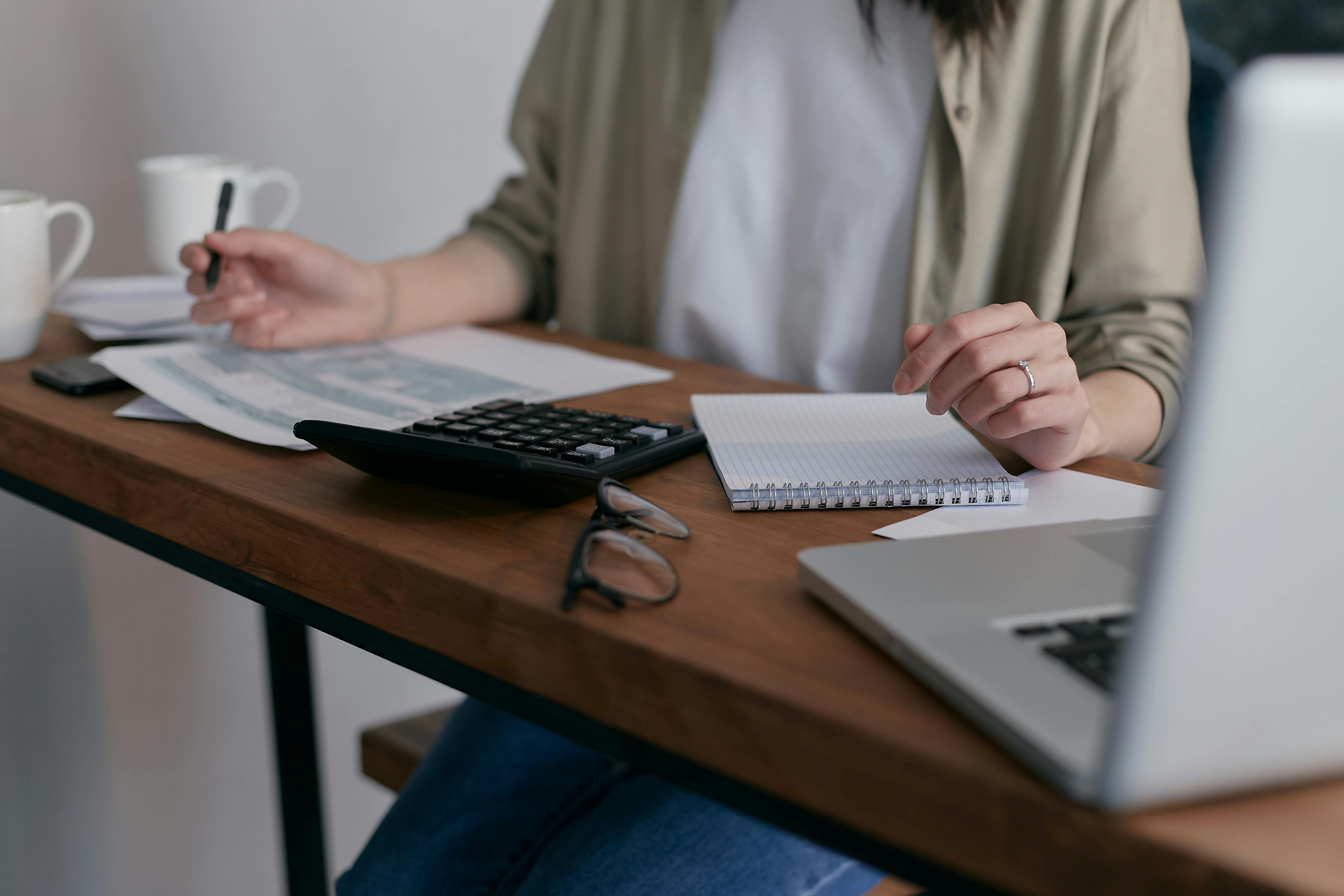 Person holding a pen sitting at a desk with papers and a calculator on it